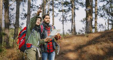 hombre y un mujer son mirando a un mapa mientras excursionismo en el bosque foto