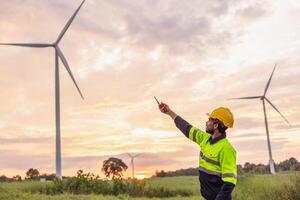 man in a yellow and black safety vest is pointing at a wind turbine photo