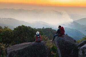 man and a woman are sitting on a rock overlooking a mountain range photo