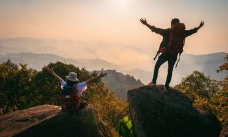 man and woman are standing on a mountain top, both wearing backpacks photo