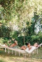 Woman resting her head on her arm on the chest of man hugging her waist while lying in a hammock in the garden photo