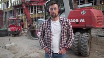 arbetstagare med bulldozer på konstruktion webbplats. manlig grävare arbetstagare. civil ingenjör workman operatör med grävmaskin i bakgrund. anställd med ett jord rör på sig maskin eller bandschaktare i främre av en byggnad. video