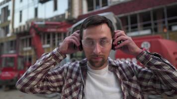 Builder in front of construction machinery puts hearing protection on ears. Worker at construction site in safety goggles and ear protection is proudly posing against heavy equipment excavator. video