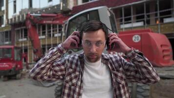 Man at work wearing safety equipment hearing protection. Construction worker ready for job puts on ear defenders to protect against sound. Male heavy equipment operator puts on protect ears. video