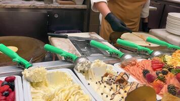 bakken pannekoeken, Aan de teller in de voorgrond ijs room, vers gemaakt pannekoeken en kleurrijk ijs room met fruit vullingen. video