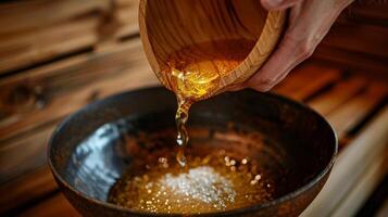 A hand pours a mixture of sea salt honey and olive oil into a bowl ready to be used as a natural scrub in the sauna. photo