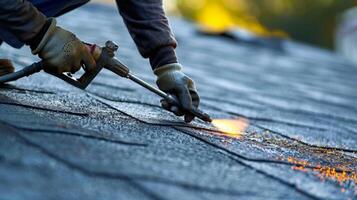 A worker using a blowtorch to melt and secure seams between different sections of roofing material photo