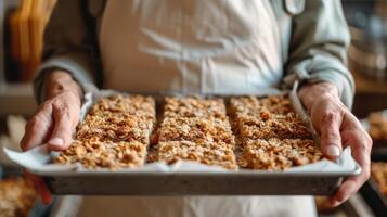 un jubilado con orgullo participación un bandeja de recién horneado Granola barras hecho con saludable avena nueces y seco frutas Listo a ser compartido con amigos y familia foto