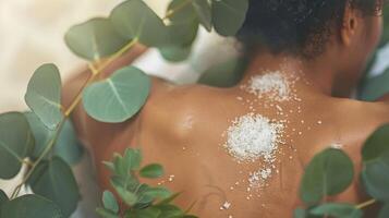 A woman luxuriates in a traditional sauna surrounded by eucalyptus leaves as a the applies a salt scrub to her back. photo