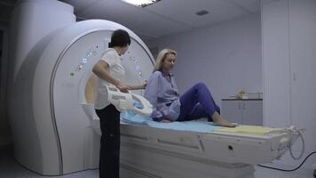 un' giovane ragazza paziente nel specializzato capi di abbigliamento cascate su un' magnetico risonanza l'imaging dispositivo video