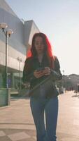 grave mujer con Delgado figura camina en ciudad parque y textos utilizando teléfono inteligente video