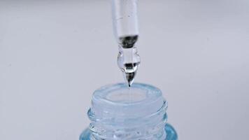 une laissez tomber de une pipette s'égoutte dans une verre bouteille fermer sur une blanc Contexte. macro lent mouvement. video