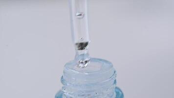 uma solta a partir de uma pipeta pinga para dentro uma vidro garrafa fechar-se em uma branco fundo. macro lento movimento. video