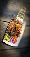 Lamb grilled satay served with barbecue savory sauce and pickled onion, chili and cucumber, selective focus photo