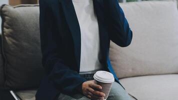 Young asian woman, digital nomad working remotely from a cafe, drinking coffee and using laptop, smiling. video