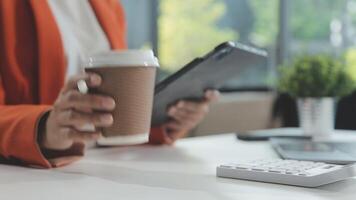 joven asiático mujer, digital nómada trabajando remotamente desde un cafetería, Bebiendo café y utilizando computadora portátil, sonriente. video