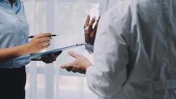 multirracial médico equipo teniendo un reunión con doctores en blanco laboratorio abrigos y quirúrgico matorrales sentado a un mesa que se discute un pacientes registros, médico equipo comprobación radiografía resultados. video