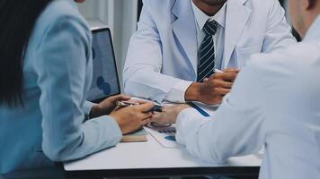 Multiracial medical team having a meeting with doctors in white lab coats and surgical scrubs seated at a table discussing a patients records, Medical team checking Xray results. video