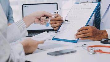 multiracial médical équipe ayant une réunion avec médecins dans blanc laboratoire manteaux et chirurgical gommages assise à une table discuter une les patients enregistrements, médical équipe vérification radiographie résultats. video