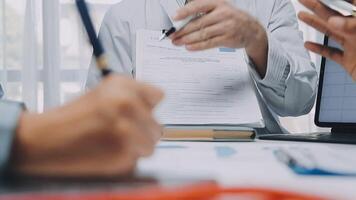 multiracial médical équipe ayant une réunion avec médecins dans blanc laboratoire manteaux et chirurgical gommages assise à une table discuter une les patients enregistrements, médical équipe vérification radiographie résultats. video