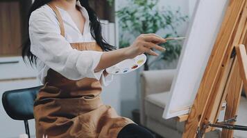 Over the shoulder selective focus shot of male artist using brush while adding color paint to pencil drawing on canvas video