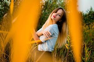 hermosa joven niña vistiendo blanco gris camiseta y negro pantalones posando en contra alto verde y amarillo césped en temprano calentar otoño. al aire libre retrato de hermosa hembra modelo foto