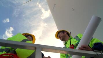 ingegneri Lavorando nel lavoro sul campo all'aperto. lavoratori dai un'occhiata e ispezionare costruzione e macchina in giro il edificio progetto luogo. vento turbine per elettrico pulito energia e ambiente sostenibilità. video