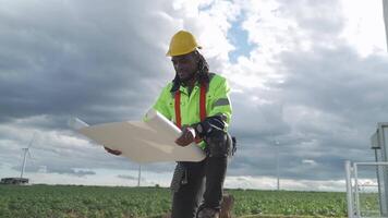 africano ingegnere Lavorando nel lavoro sul campo. lavoratore seduta e ispezionare costruzione e macchina in giro il progetto luogo. vento turbina elettrico di pulito risorsa energia e ambiente sostenibile. video