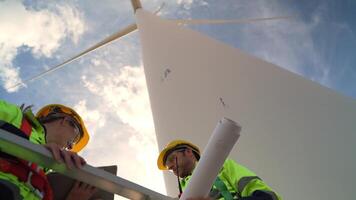 ingenieros trabajando en trabajo de campo al aire libre. trabajadores cheque y inspeccionar construcción y máquina alrededor el edificio proyecto sitio. viento turbinas para eléctrico limpiar energía y ambiente sostenibilidad. video