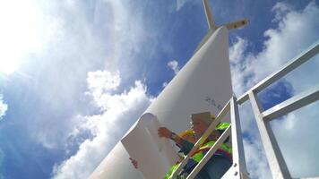 ingenieros trabajando en trabajo de campo al aire libre. trabajadores cheque y inspeccionar construcción y máquina alrededor el edificio proyecto sitio. viento turbinas para eléctrico limpiar energía y ambiente sostenibilidad. video