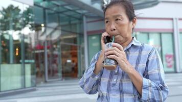 Asian senior old woman is drinking coffee and walking around outdoor pedestrian. video