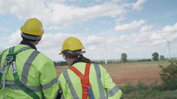 ingenieros trabajando en trabajo de campo exterior. trabajadores caminando y inspeccionar construcción y máquina alrededor proyecto sitio. viento turbina eléctrico de limpiar recurso energia y ambiente sostenible. video