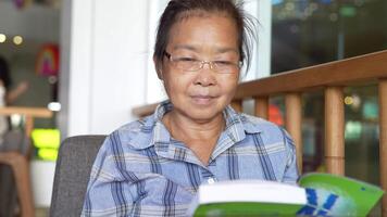 asiatique Sénior vieux femme est en train de lire livre. video