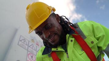 africano hombre trabajadores Ingenieria sentado con confianza con azul trabajando traje vestir y la seguridad casco en frente de viento turbina. concepto de inteligente industria trabajador operando de renovable energía. video