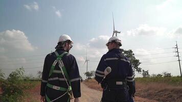 ingenjörer man och kvinna inspekterande och gående av vind turbin odla. vind turbin med ett energi lagring systemet drivs förbi super energi företag. arbetare möte till kolla upp runt om de område. video