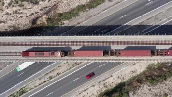 antenne visie van een vracht trein in beweging over- een bezig snelweg 4k achtergrond video