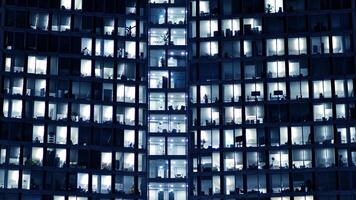 fragmento de el vaso fachada de un moderno corporativo edificio a noche. moderno vaso oficina en ciudad. grande brillante ventanas en moderno oficina edificios a noche, en filas de ventanas ligero brilla foto