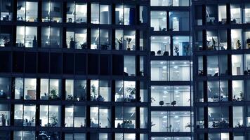 Fragment of the glass facade of a modern corporate building at night. Modern glass office in city. Big glowing windows in modern office buildings at night, in rows of windows light shines. photo