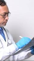 verticale, un' medico è guardare a un' ct scansione di un' del paziente testa. il medico è indossare un' bianca laboratorio cappotto e blu guanti video