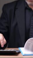 A man is sitting at a desk with a calculator and a receipt. He is focused on the numbers on the receipt, possibly trying to calculate a total or check for errors video