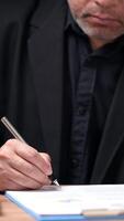 uma homem dentro uma terno é escrevendo com uma caneta em uma peça do papel. conceito do profissionalismo e formalidade, Como a homem é vestido dentro uma terno e escrevendo em uma formal documento video