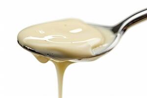 Stainless steel ladle dripping with creamy alfredo sauce, isolated against a stark white background photo