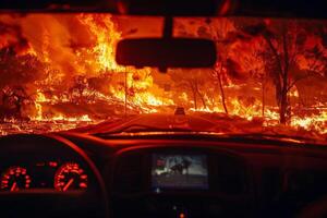 View from inside a car evacuating from a wildfire area, flames visible through the rear window photo