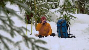 A man sits in the snow in the winter forest. Winter sports and recreation hiking concept. Carpathian mountain range. 4K video