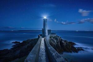 Large retro lighthouse with beam of bright light shining out to blue sea photo