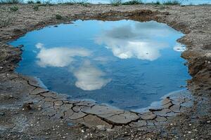 lago el secado arriba en un ola de calor, agrietado tierra y pequeño charcos izquierda, reflejando duro ambiental condiciones foto