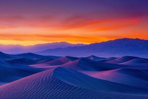 Sunrise paints unusual fractal patterns on undulating desert sand dunes with a vibrant orange and purple gradient sky as backdrop photo