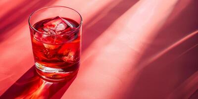 Iced red cocktail in a clear glass set against a vibrant pink surface, invoking concepts of summer refreshments and celebratory toasts photo