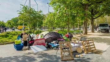 Temporary street shelter with personal belongings in a sunny Paris park, capturing urban poverty and homelessness in Paris, France, April 14th, 2024 photo