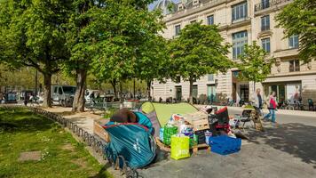 Springtime in Paris, France, April 14th, 2024, showcasing urban life with an apparent homeless encampment juxtaposed against a backdrop of bustling city activity and greenery photo